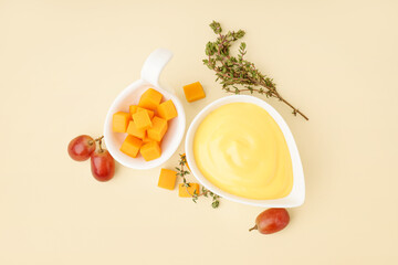 Bowl with tasty cheddar cheese sauce, thyme and grapes on beige background