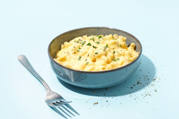 Bowl of tasty Italian pasta with Cheddar cheese on blue background