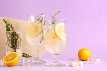 Glasses with fresh lemonade and rosemary on lilac background