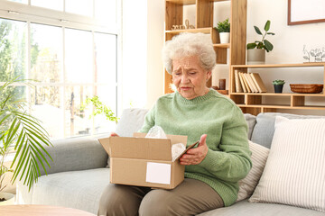 Upset senior woman opening parcel at home