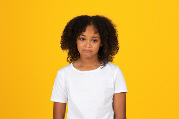 Sad upset teen curly african american girl in white t-shirt looking at camera, isolated yellow...