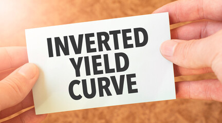 INVERTED YIELD CURVE word inscription on white card paper sheet in hands of a businessman. recap...