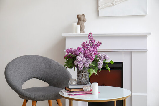 Vase with lilac flowers, books and candles on table in living room