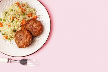 Cutlets with bulgur, boiled vegetables and fork on pink background