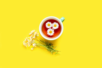 Cup of natural chamomile tea and flowers on yellow background