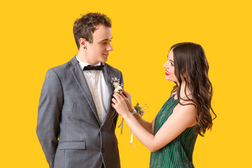 Beautiful prom couple pinning boutonniere on yellow background