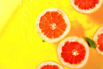 Slices of fresh grapefruit and leaves in water on yellow background