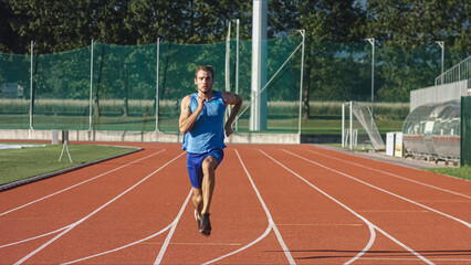 Caucasian male athlete in blue sportswear running alone along an athletic track on the stadium