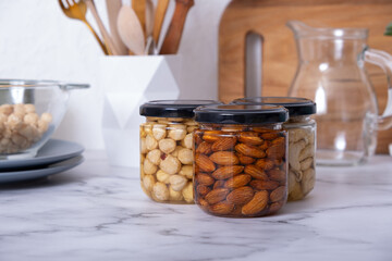 Glass jars with honey and nuts. Almonds, hazelnuts and cashew in honey in kitchen interior