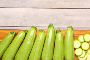 Board with many fresh green zucchini on grey wooden background