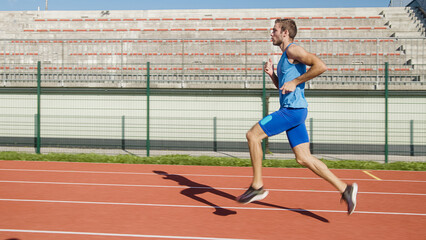 Caucasian male professional racer running along an athletic track on the stadium, tracking side shot.