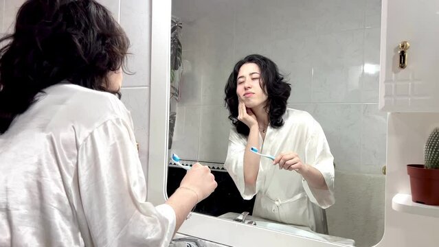 video of portrait of a latin woman holding a toothbrush looking at her molars and teeth in the mirror. oral hygiene problems in young people is very common
