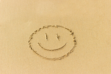 Funny smiley face drawn on the wet sand of the beach. Concept of happiness, vacation.