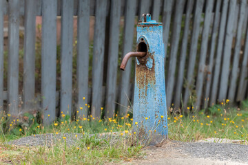 An old water column with blue cracked paint in the village. Close-up of a drinking water supply column.