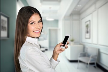 Smiling young business woman holding phone working in office