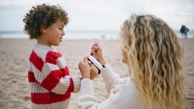 Mother helping flying kite on beach closeup. Smiling adorable son holding thread