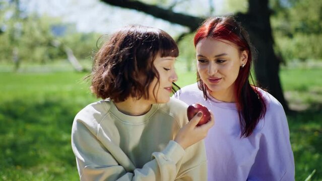 Good looking two lesbian ladies in the park have a picnic they eating together one apple and enjoy the sun together