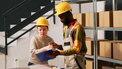 Supervisor signing shipment papers in depot, reviewing list of merchandise to prepare retail store order. Man and woman verifying delivery logistics in storage room. Handheld shot.