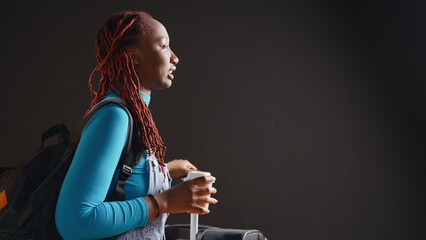 Joyful person with coffee cup waiting for airplane, preparing to leave and go to urban destination. Young woman drinking refreshment before travelling on international trip. Handheld shot.