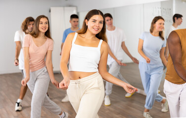 Group of sportive young adult diverse dancers performing dynamic movements during aerobic dance workout in gym