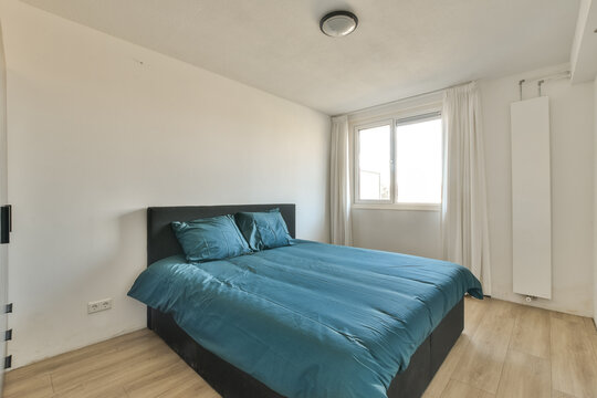 a bedroom with wood flooring and blue comforter on the bed in front of the window looking out to the city