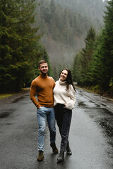 lovers laugh and embrace walking on a wet road in a mountainous area. autumn walk of a guy with a girl. joint trip