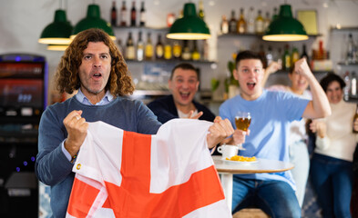 Group of friends, sports supporters cheering for favorite team with flag of England while watching...