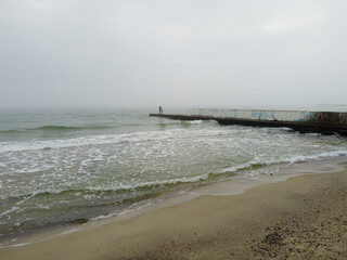 A Black see coast during a low tide and two people standing on a pier.