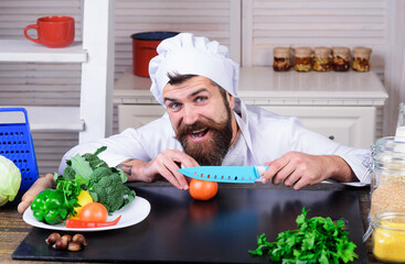 Male chef preparing tasty fresh vegetable salad. Chef with sharp knife cuts tomato. Diet, healthy food cooking, vegetarian concept. Professional chef in cook uniform in kitchen preparing vegan salad.
