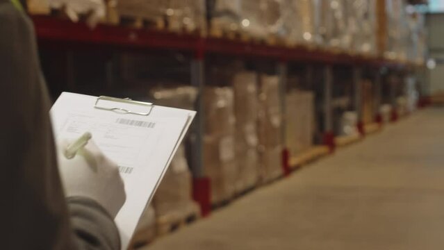 Midsection of unrecognizable warehouse manager with invoice papers on clipboard walking along aisle doing inventory management