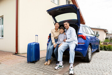 Happy young african american family of three sitting together in car trunk, ready for summer...