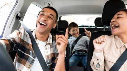 Happy diverse family of three riding car and singing, having fun traveling together by automobile,...
