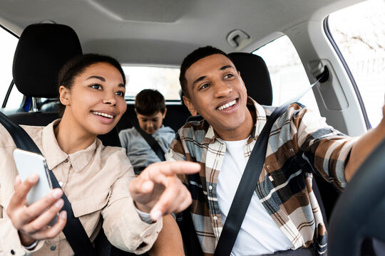 Happy Diverse Family Sitting Inside Luxury Car, Using Digital Map Application, Woman With Mobile Phone Pointing At The Road, Showing Way