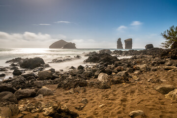 Wavy ocean in Mosteiros coast Sao Miguel island Azores archipelago Portugal. Ponta do Castelo. Silky water during longer exposure, blured branches. Stones and rocks in foreground
