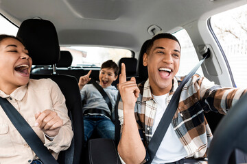 Excited young african american family singing riding new car and having fun enjoying summer road...