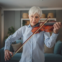 Mature senior caucasian woman learn to play violin practice at home