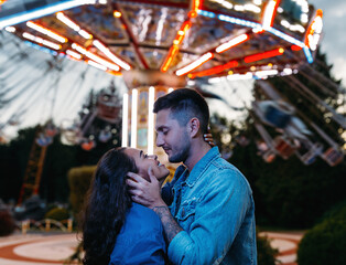 Obraz na płótnie Canvas Happy couple in an amusement park. Young couple in love hugging and looking at each other against the carousel.