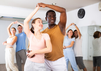 Positive smiling dancing couple enjoying active dancing during group training in dance hall