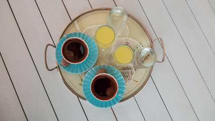 Two cups of turkish coffee served with a little cookie and lemon liqueur or  limoncello  on tray on white wooden table