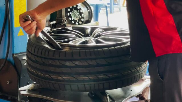 A skilled mechanic is putting new car tires on alloy wheels.
