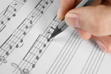 Woman writing musical notes with pencil on sheet of paper, closeup