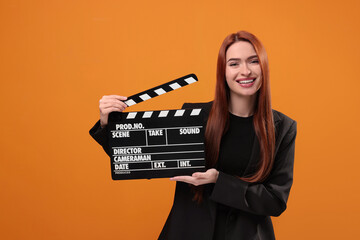 Happy actress with clapperboard on orange background. Film industry