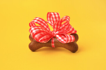 Bone shaped dog cookie with red bow on yellow background, closeup