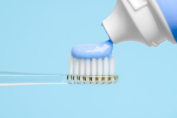 Squeezing toothpaste onto electric toothbrush on light blue background, closeup