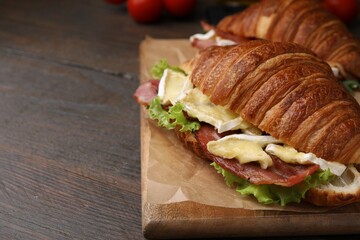 Tasty croissant with brie cheese and bacon on wooden table, closeup. Space for text