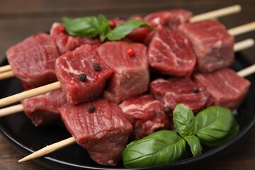 Wooden skewers with cut fresh beef meat, basil leaves and spices on table, closeup