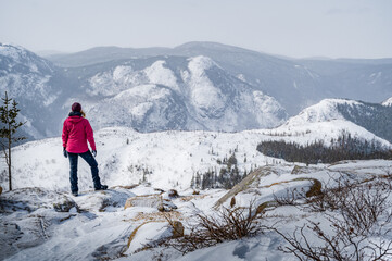 Standing female hiker over the horizon, admiring the surrounding mountains under the snow,...