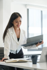 Millennial female manager standing at office desk and looking at laptop screen.