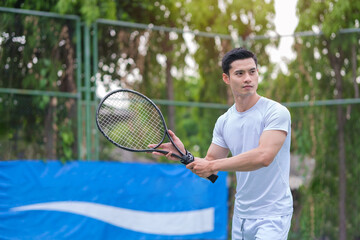 Handsome male athlete holding tennis racket and looking concentrated while standing on tennis court.