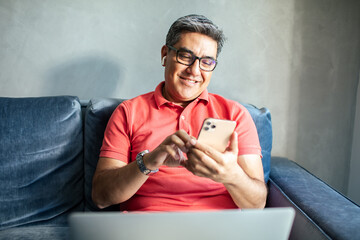 MIddle aged latin man using a smart phone on a couch at home